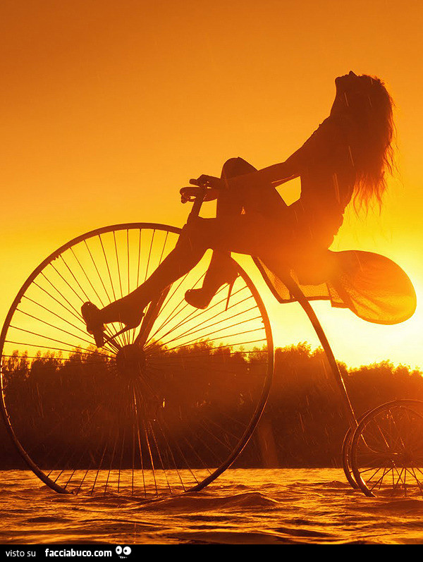 Sulla bicicletta dalla ruota enorme al tramonto